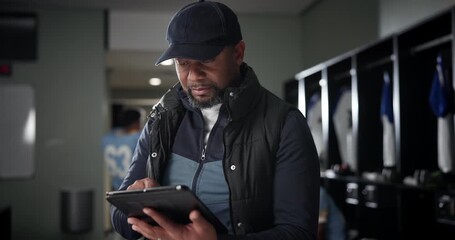 Black man, football coach and tablet with team in locker room for strategy, game plan or sports news. African mentor, athlete or trainer scrolling or browsing on technology before match or playoffs - Powered by Adobe