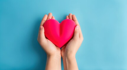 Obraz premium Hands carefully holding a red heart against blue backdrop 