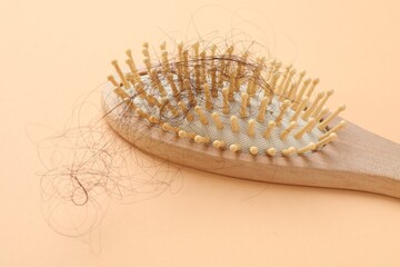 One brush with lost hair on beige background, closeup. Alopecia problem
