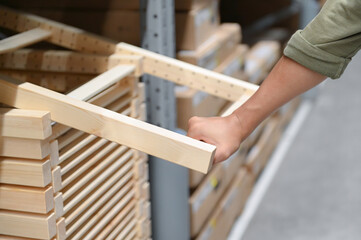 Hand of a person selecting a wooden item from a shelf in a warehouse, illustrating attention to detail. The scene captures a close-up view of the hand.