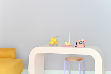 Minimalist room with a white table, yellow chair, pastel colored decor items, and a gray wall.