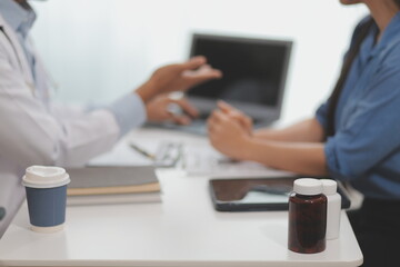 Doctor and patient sitting near each other at the wooden desk in clinic. Female physician's pointing to a records form. Medicine concept