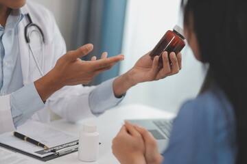 Doctor and patient sitting near each other at the wooden desk in clinic. Female physician's pointing to a records form. Medicine concept