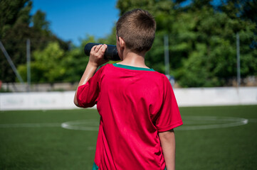 Boy in red football uniform playing soccer, football on field, outdoors.