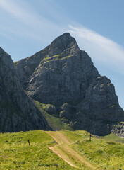 A grassy road winds through a meadow and toward a cliff face in Lofoten, Norway
