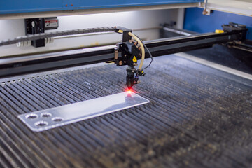 Closeup industrial CO2 laser cutting machine working with high powered red laser beam on acrylic or...
