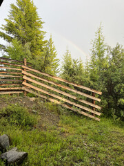 Wooden fence in the forest with a rainbow in the sky.