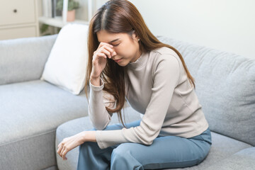 Depressed anxiety asian young woman, girl frustrated closed eyes, touching nose suffering stressed, sick, tired, crisis sitting on sofa from headache, migraine pain tension problem health care concept