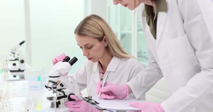 Scientist using microscope examines medical samples colleague, laboratory assistant writes down the test results