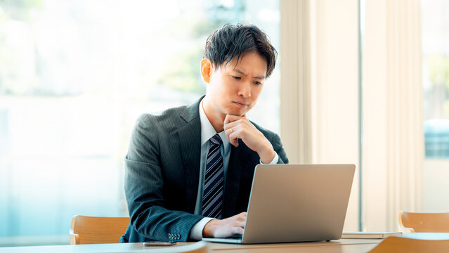パソコンを使いながら考える日本人男性ビジネスマン