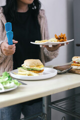 Hand holding a plate of fries and sausages as a side dish of burgers