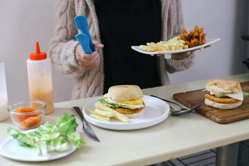 Hand holding a plate of fries and sausages as a side dish of burgers