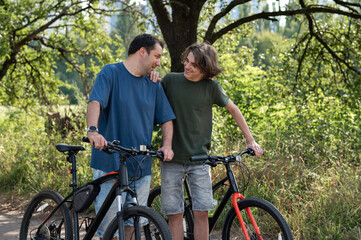 Obraz premium Father and teenager son talking and smiling while walking outdoor in park with bicycles