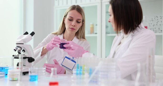 Scientist gives purple liquid to young intern in chemistry laboratory
