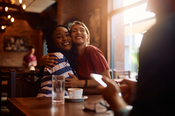 Happy female friends embracing while gathering in café.