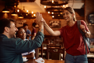 Happy friends greeting while gathering in café.