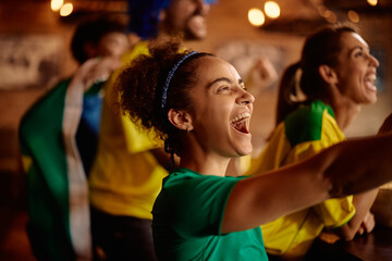 Cheerful sports fan watching a match with her friends in pub.