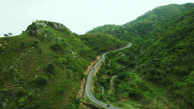 4k Scenic aerial view of vehicles on the road through green hills of Rayta at Udaipur, Rajasthan, India. Road trip through a forest. Transportation Aerial view of bikes driving on scenic hilly road