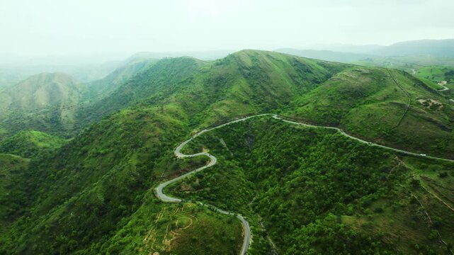 4K shot of vehicles passing on scenic road in mountains and clouds in sky at Rayta in Udaipur, Rajasthan, India. Monsoon clouds and green hills of Rayta. Tourism and holidays background.