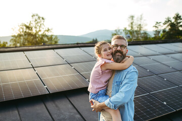 Father with girl on roof with solar panels, hugging, looking at camera. Rooftop solar or...