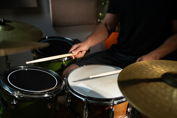 A close-up view of a drummer's hands as they play a snare drum during a practice session. The drummer is wearing a black t-shirt and is sitting behind a drum set