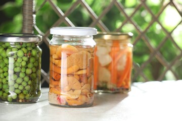 Tasty pickled vegetables and mushrooms in jars on white table indoors