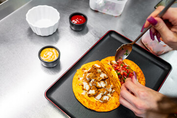 A person preparing tacos with chicken and salsa on a black tray, with sauces on the side. The image highlights fresh ingredients and meal preparation.