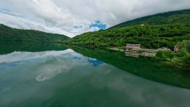 Lago di levico with lush green hills and calm waters on a cloudy day, aerial view