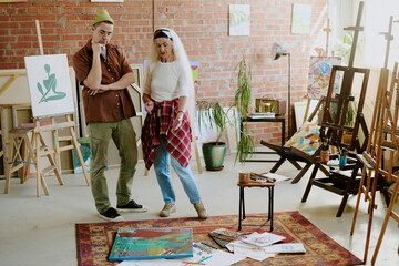 Naklejka premium Two diverse artists standing in studio, looking at abstract acrylic painting and giving comments, copy space