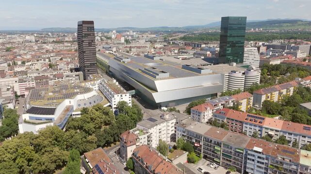 Basel's messe building with cityscape and forward-moving truck on a sunny day, aerial view