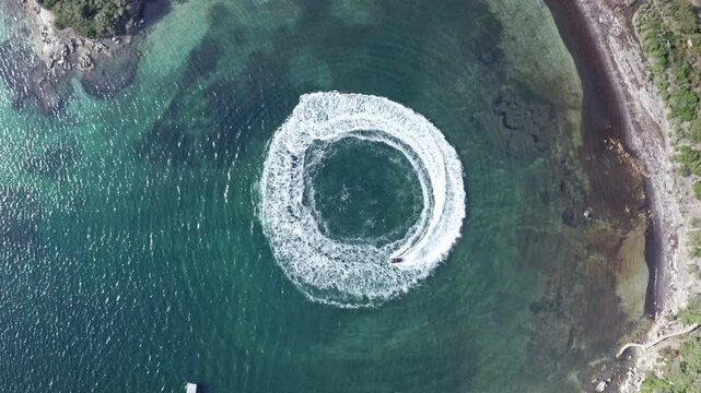 Boat creating a perfect circle in turquoise waters of Sardinia, aerial view