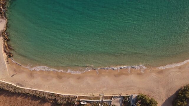 Drone top down rising from pristine golden sand beach with clear turquoise blue ocean water waves crashing on shore in Donousa Greece