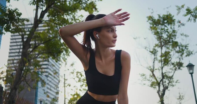 Amidst urban run woman athlete pauses for moment of respite by park. With gentle breeze cooling woman skin she savors serenity of surroundings using break to recharge and refocus her energy.