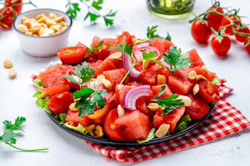 Juicy salty sweet summer salad with watermelon, tomatoes, onion, peanuts and parsley on white background, top view