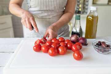 Woman cutting cocktail tomatoes in half on a cutting board in the kitchen