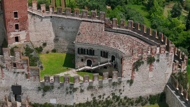 Aerial overhead view of medieval castle features a courtyard and tall crenellated walls surrounded by vibrant greenery, showcasing historic architecture and a serene, natural landscape.