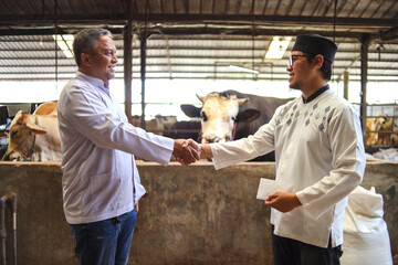 Side View Of Asian Muslim Man Shaking Hands In Cattle Farm After Buying A Cow in Preparation for...