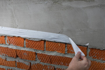 A person is holding a roll of tape and is about to apply it to a brick wall