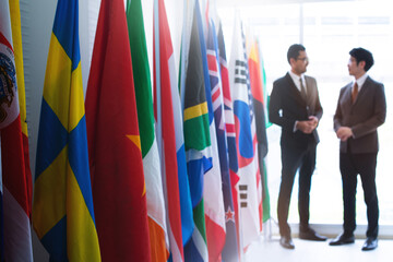 Businessmen attending an international seminar greet each other at the end of a row of flags,.flags from many countries lined up along the walkway, selective focus © chomplearn_2001