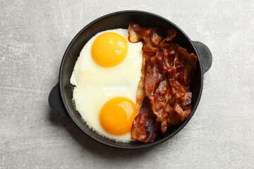 Tasty bacon and eggs in dish on gray textured table, top view