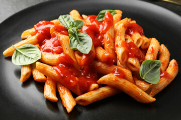 Delicious pasta with tomato sauce and basil on black plate, closeup