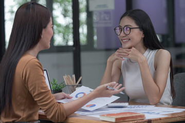 Two young Asian businesswomen discussed investment project work and planning strategy. Business people talk together on laptop computers at the office.