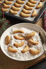 Praparation of homemade Christmas cookies called Kipferl - coating freshly baked crescents in suger with vanilla