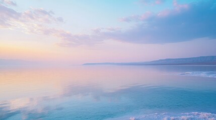 The tranquil waters of the Dead Sea, reflecting the pastel hues of the early morning sky, surrounded by salt formations.