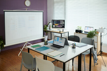 Contemporary office environment showcasing a neatly arranged meeting space with laptop setups on desks and a projection screen in background for presentations