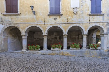 a stone plaza with several columns with flowers and buildings behind