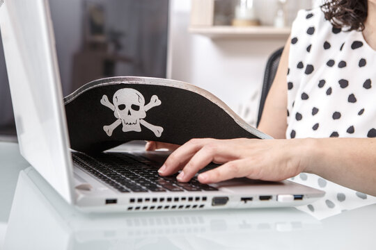 A person engages in online activities in a workspace, wearing a pirate-themed hat with a skull and crossbones. The person is focused on his laptop, highlighting the ongoing concern about hacking and t