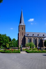 Photo of an orthodox church in the village of Kessel in Germany. With a small square and a waterfall in front of it. Under a blue sky.