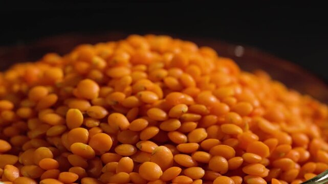 Raw red lentils are scattered out of the glass bowl.