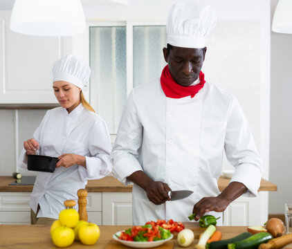 Professional chef in white uniform working with female assistant in private kitchen
